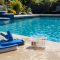 Pool brush vacuum head and water test kit beside a clear backyard swimming pool