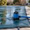 Automatic pool cover pump and discharge hose set on a rain-wet swimming pool safety cover before a storm
