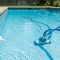 Suction-side pool cleaner hose near an adjustable return jet in a clear backyard pool